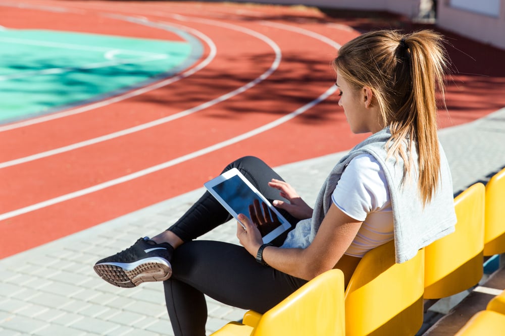 Portrait of a fitness woman resting with tablet computer at outdoor stadium